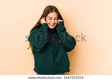 Young caucasian woman isolated en beige background covering ears with hands.