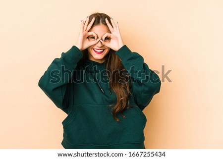 Young caucasian woman isolated en beige background showing okay sign over eyes