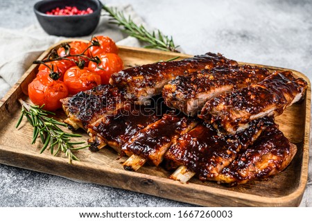 Delicious barbecued ribs seasoned with a spicy basting sauce and served with baked tomatoes. Gray background. Top view Royalty-Free Stock Photo #1667260003