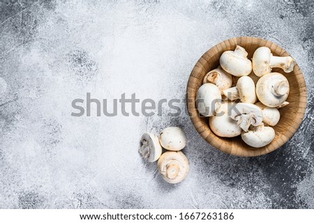Raw white mushrooms in a bamboo bowl. Gray background. Top view. Space for text
