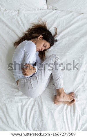 Top view of sick young woman lying in bed touch belly suffer from stomach ache, ill millennial girl struggle with periods pain, having eating disorder or indigestion trouble, health problem concept Royalty-Free Stock Photo #1667279509
