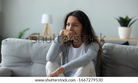 Unhappy millennial girl sit on couch in living room look in distance thinking pondering of problems, upset sad young woman lost in thoughts suffer from depression at home, psychological trauma concept Royalty-Free Stock Photo #1667279530
