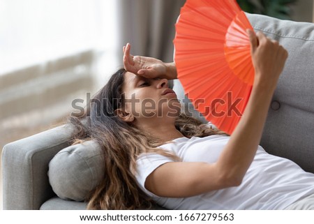 Exhausted young woman lying on couch in living room using hand fan feeling sick at home, tired millennial girl waving with hand waver suffer from heatstroke, lack of fresh air, no air conditioner Royalty-Free Stock Photo #1667279563