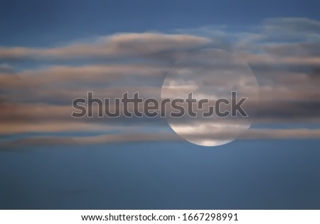 The big full moon in the blue sky behind the clouds out of focus in the early morning. Natural background with space for copy and design.