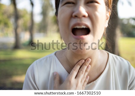 Close up of hands touching neck,sick asian girl has strong sore throat,cough,hoarseness,laryngeal cancer,swelling,young woman suffering from throat problems,tonsillitis,painful swallowing,health care Royalty-Free Stock Photo #1667302510