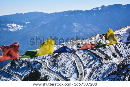 Zig zag roads of snow covered Sela pass with Buddhist prayer flags in the foreground. Royalty-Free Stock Photo #1667307208