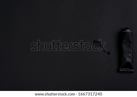 Black paint tin tube squeezed isolated on dark background. Top view.