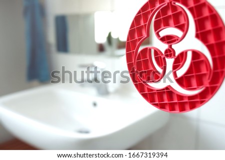 red 3D printed sculpture with biohazard symbol in front of a bright bathroom sink at home - epidemic, personal hygiene and health concept