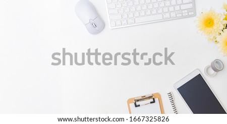 Flat lay blogger or freelancer workspace with a keyboard, flowers in a vase, office supplies on a light background