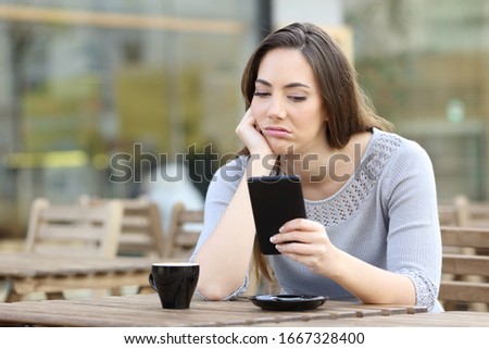 Bored girl looking disappointed at her smart phone on a cafe terrace Royalty-Free Stock Photo #1667328400