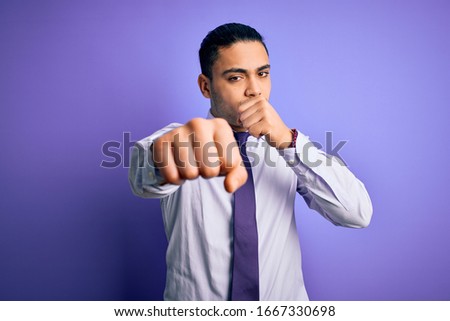 Young brazilian businessman wearing elegant tie standing over isolated purple background Punching fist to fight, aggressive and angry attack, threat and violence