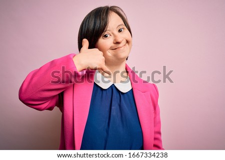 Young down syndrome business woman over pink background smiling doing phone gesture with hand and fingers like talking on the telephone. Communicating concepts.