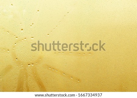 hand draws a sun on a glass window with drops background