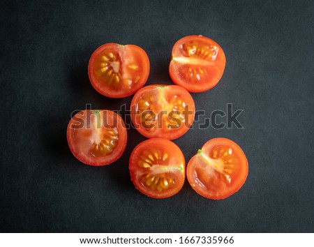 Sliced cherry tomatoes on black wooden board, high resolution photo .