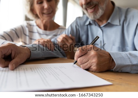 Close up of 60s husband and wife sit at desk sign health insurance contract close deal, smiling old mature couple spouses put signature on document make good agreement, elderly healthcare concept Royalty-Free Stock Photo #1667343250