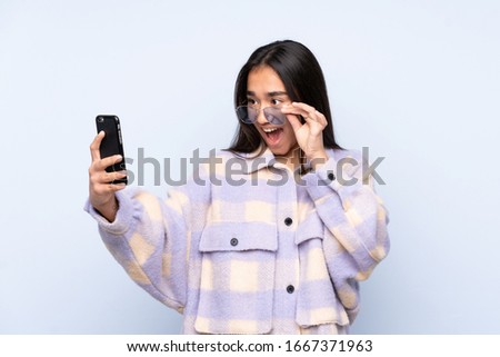 Young Indian woman isolated on blue background making a selfie