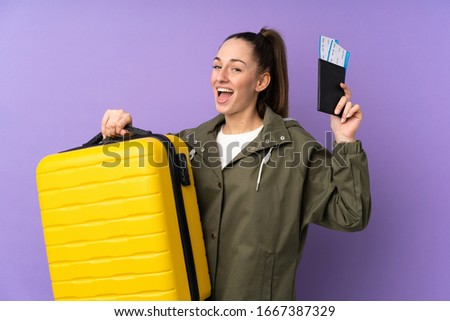 Young brunette woman over isolated purple background in vacation with suitcase and passport