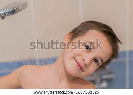 Close-up portrait of cute little boy in bathroom with shower. Little boy is bathed in the shower