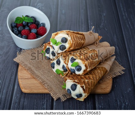 waffles rolled up with cream and fresh berries on a dark background
