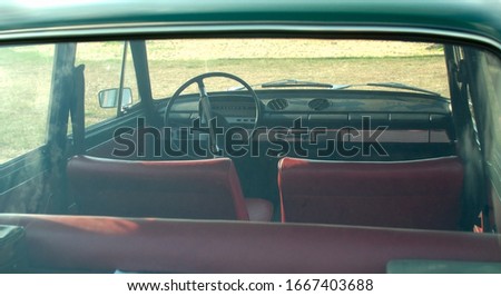 Vintage car interior with red seats and big steering wheel view through the rear window in retro style