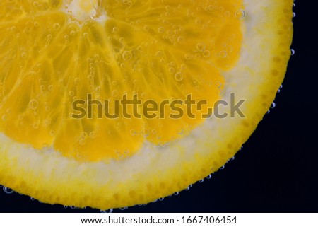 Close-up of a fresh slice of an orange floating underwater with air bubbles and producing fresh lemonade.