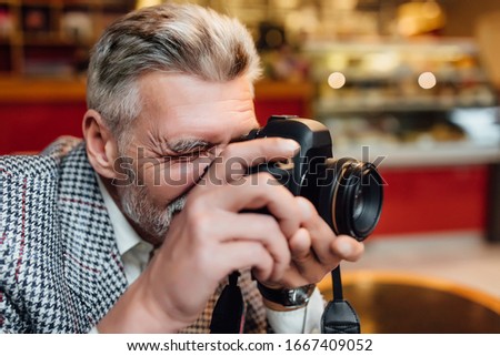 Senior man photographer is holding an old photocamera and make a pictures at modern cafeteria.