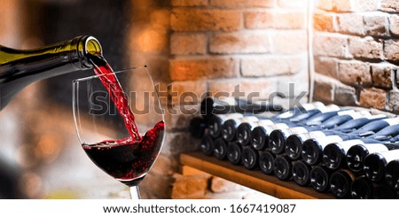 Pouring red wine into the glass against rustic background. 