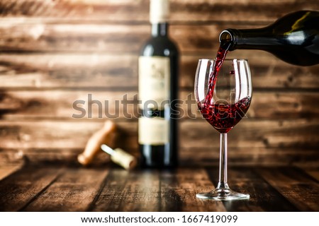 Pouring red wine into the glass against rustic background.  Royalty-Free Stock Photo #1667419099