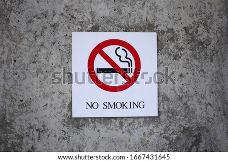 No smoking sign in a public outdoor area with grey wall background.