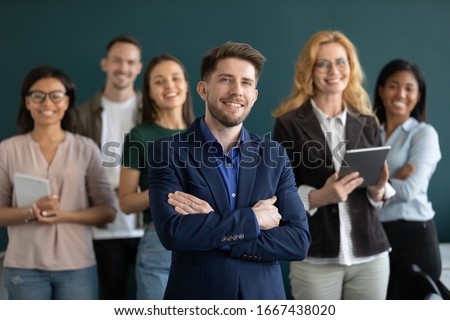 Group picture of successful millennial male boss CEO stand forefront pose with multiracial colleagues in office, diverse company businesspeople look at camera show unity support, leadership concept Royalty-Free Stock Photo #1667438020