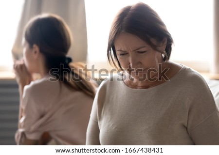 Head shot offended middle aged desperate woman sitting separately on couch with ignoring grownup daughter on background. Frustrated unhappy senior mature mother feeling despair after quarrel. Royalty-Free Stock Photo #1667438431
