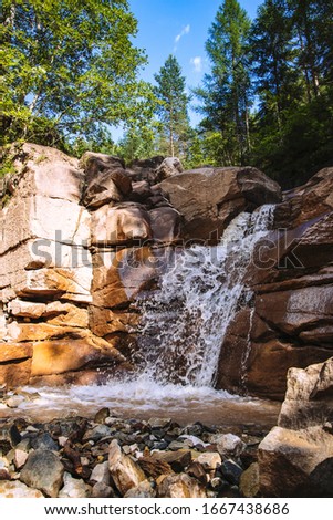 small waterfall that flows into a stream of water with many rocks around it