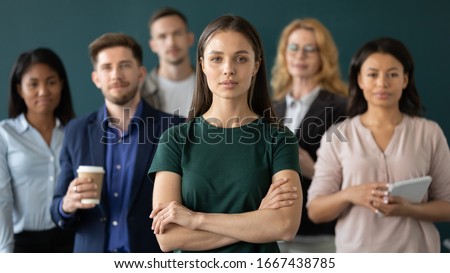 Successful millennial businesswoman stand forefront of multiracial team posing together in office, confident young Caucasian female boss or leader with multiethnic colleagues lawyers at workplace Royalty-Free Stock Photo #1667438785