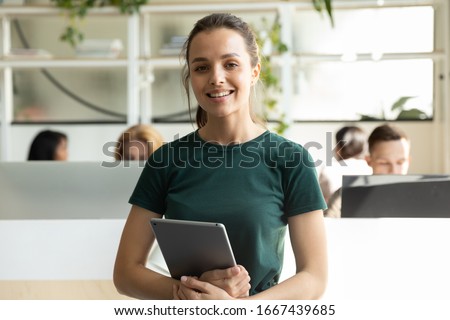Portrait of smiling millennial Caucasian girl graphic designer pose holding modern tablet, profile picture of happy young female employee worker stand with pad in coworking office, internship concept