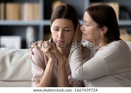 Compassionate middle aged mother comforting stressed upset daughter, sitting together on sofa at home. Kind senior mature mommy supporting soothing frustrated desperate unhappy grownup child. Royalty-Free Stock Photo #1667439724