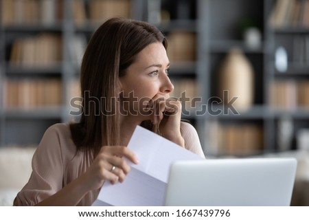 Head shot stressed young woman holding paper document, bank debt notification, thinking of financial troubles, looking away. Lost in negative thoughts depressed woman worrying about bad news notice. Royalty-Free Stock Photo #1667439796