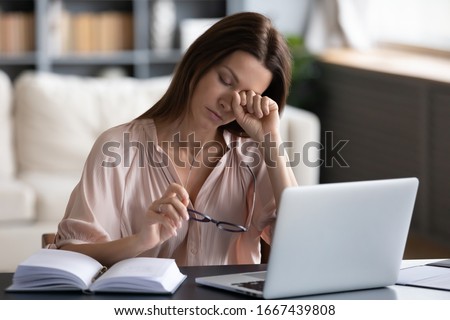 Overwhelmed unhappy young woman taking off glasses, rubbing eyes, feeling exhausted, working remotely on computer at home. Tired stressed lady suffering from dry eyes syndrome, massaging nose bridge. Royalty-Free Stock Photo #1667439808