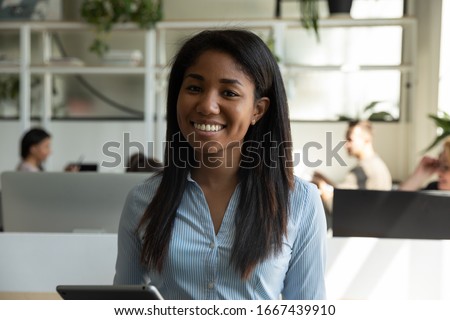 Profile picture of smiling African American millennial female employee posing in coworking space holding tablet, headshot portrait of happy biracial woman worker stand in office, internship concept