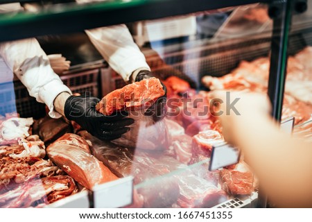 Close up on butcher's hands in gloves working in butchery. Royalty-Free Stock Photo #1667451355