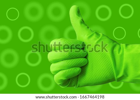 Hand in green protective rubber glove on green background with dots. Approved gloved hand thumbs up and showing ok. Concept of sanitation and hygiene