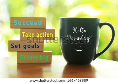 Hello Monday. Inspirational quote - Dream big. Set goals. Take action. Succeed. With colorful positive motivational words on wooden blocks and morning cup of coffee closeup.