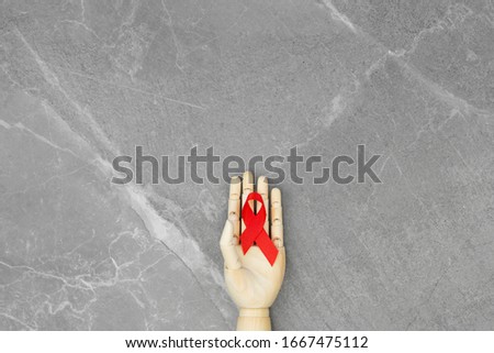 Wooden hand with AID red ribbon in it, on gray marble isolated background. Cancer Control Concept. Symbolizing day of AIDS and HIV