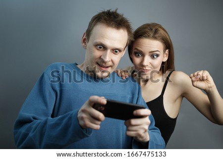 Man with the girl excitedly looking at the smartphone on gray isolated background. Concept of playing on the phone in an agitated state. Emotions of experiencing joy and excitement Studio photo