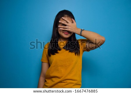 Portrait of Young beautiful asian women with blue isolated background, looking through fingers with embarrassed expression