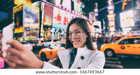 New York city tourist selfie Asian happy woman taking photo at night in Times Square, Manhattan, USA. Girl traveler joyful and smiling. Multiethnic in her 20s.