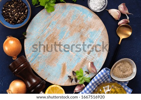 Flat lay of round cutting board and cooking ingredients on blue background