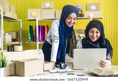 Portrait of smiling beautiful two muslim owner asian woman freelancer sme business online shopping working on laptop computer with parcel box on table at home - Business online shipping and delivery 