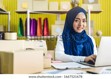 Portrait of smiling beautiful muslim owner asian woman freelancer sme business online shopping working on laptop computer with parcel box on table at home - Business online shipping and delivery 