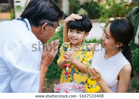 Mother teach her son to pay respect to grandpa by press the hands together at the chest with jasmine garland as a traditional activity in Thai family day. Royalty-Free Stock Photo #1667533408