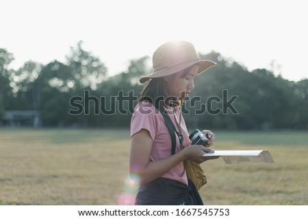 Closeup portrait of happy beautiful young adventurous woman in casual clothes with hat, camera and map is looking at camera in forest while walking and hiking for camping on epic mountain. 